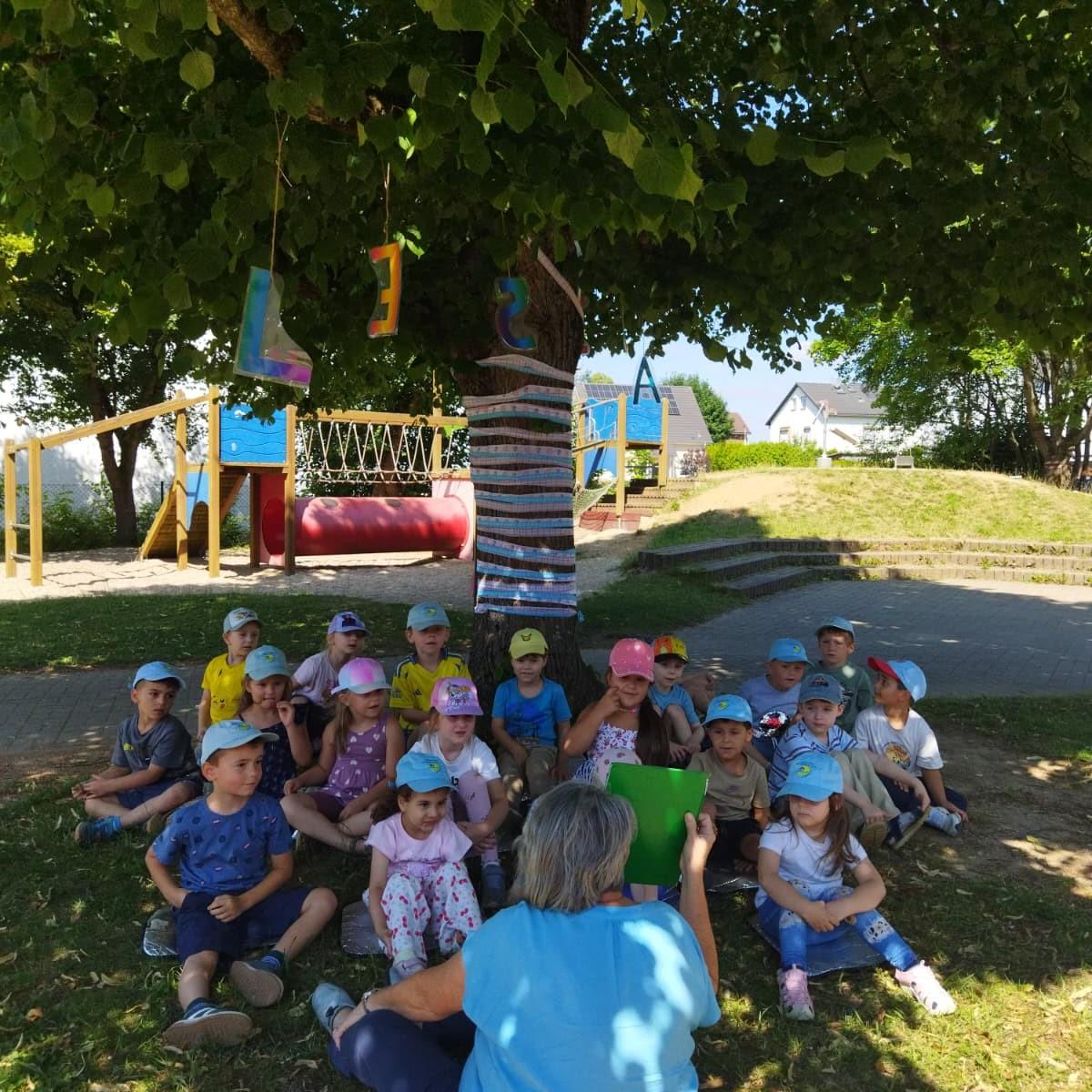 Die Kinder hören eine Geschichte unter dem Lesebaum