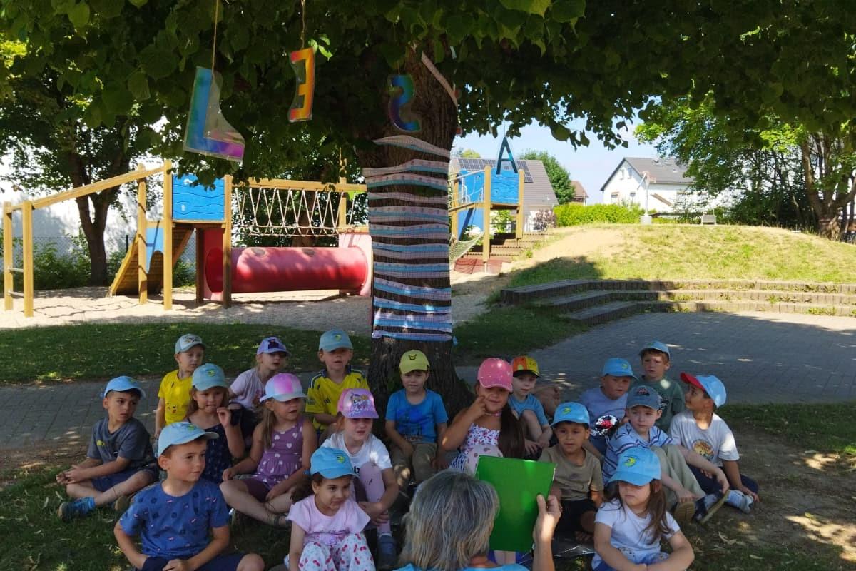 Die Kinder hören eine Geschichte unter dem Lesebaum